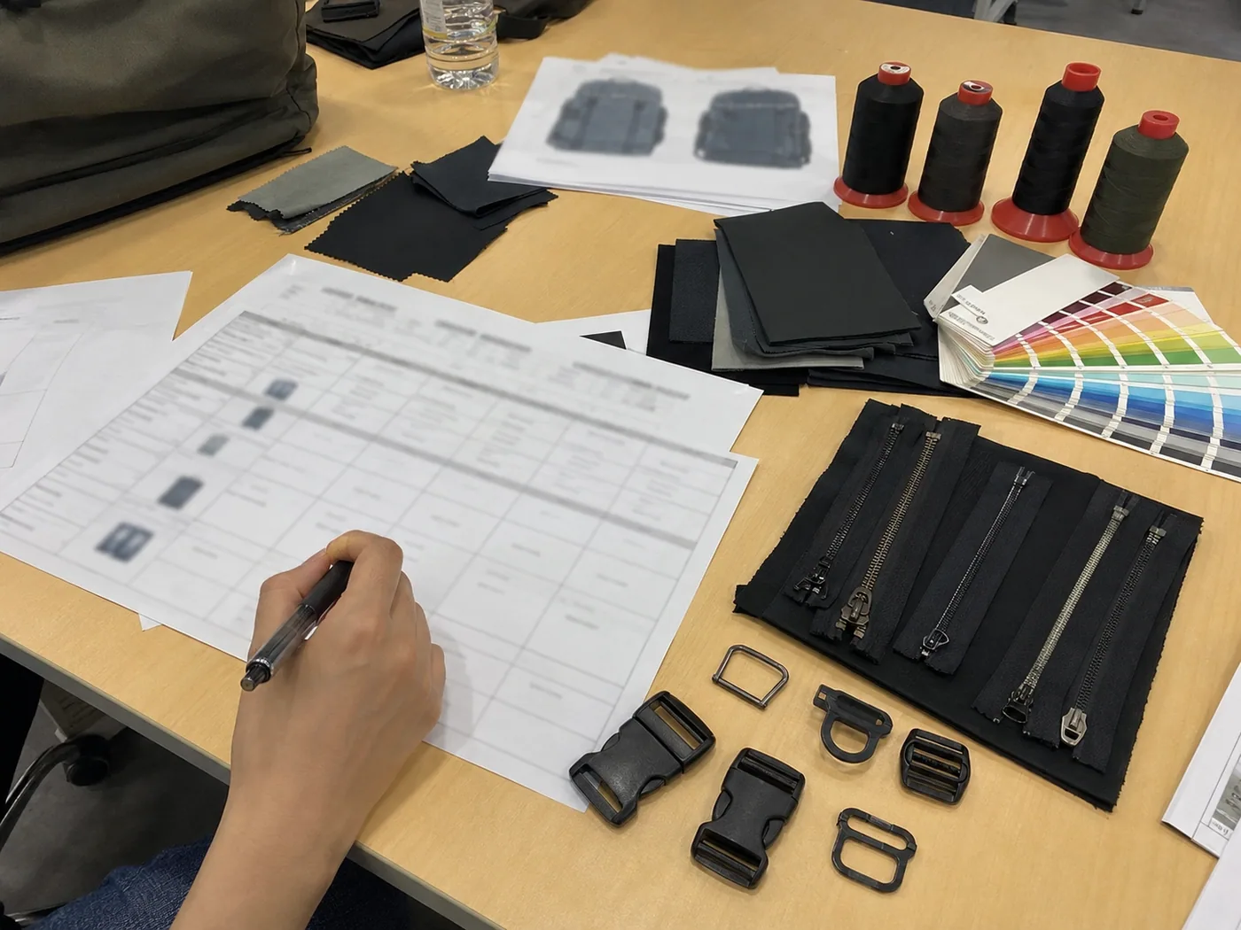 Smartphone-style custom bag MOQ planning desk with calculator, swatches, zipper roll, buckle tray, and sample tote