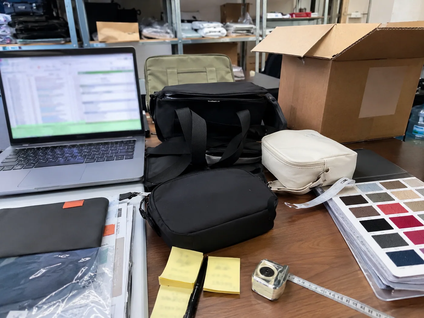 Smartphone-style supplier comparison desk with bag samples, swatches, supplier notes, carton sample, and measuring tape