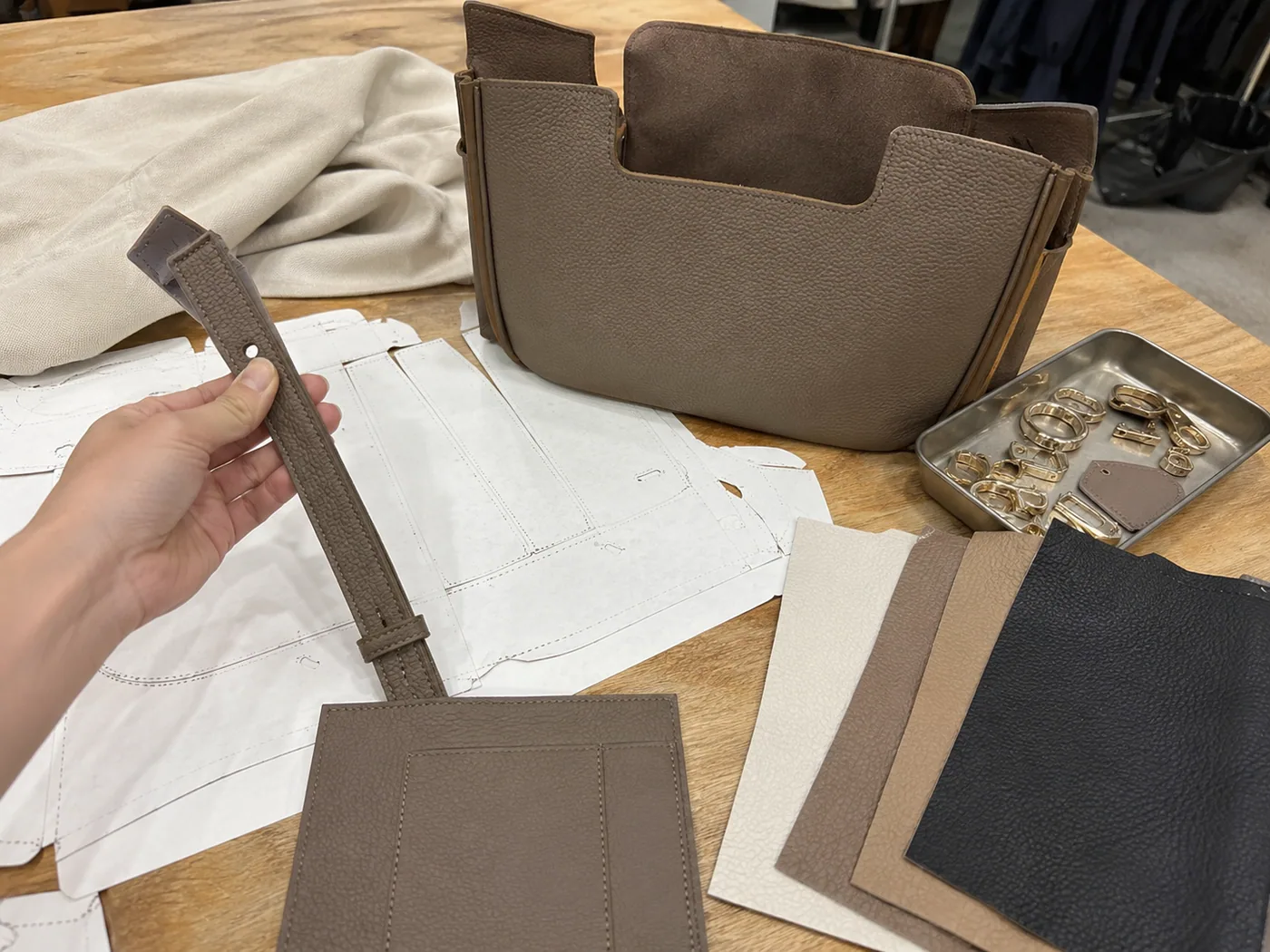 Smartphone-style handbag prototype development with paper pattern pieces, unfinished handbag body, swatches, lining, hardware tray, and strap