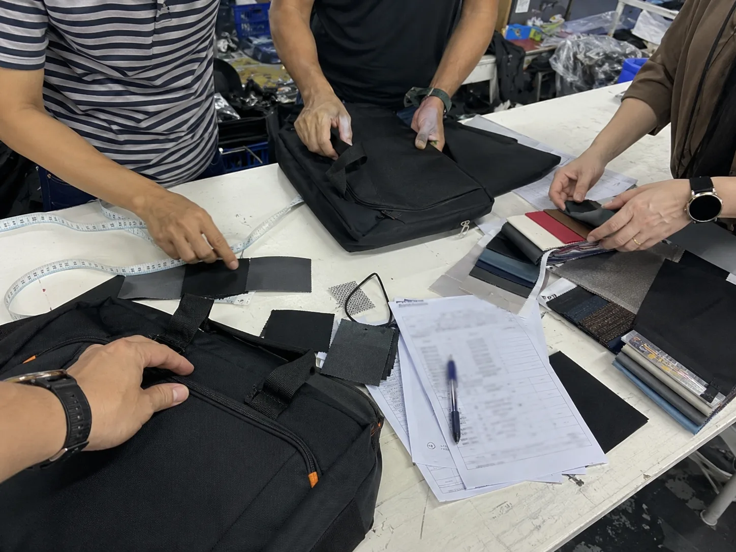 Factory team reviewing bag samples, swatches, and measurement notes at a workbench
